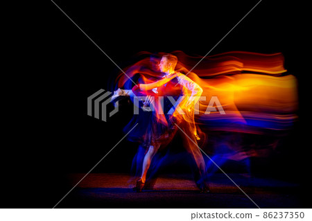 Dynamic portrait of young ballroom dancers dancing Argentine tango isolated on dark background with neon mixed light. 86237350