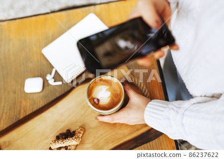 Woman hands taking a picture of a coffee cup with smart phone and laptop at a coffee shop.  86237622