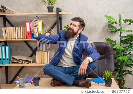 Happy boss smile to smartphone sitting cross-legged on office desk, selfie 86237767
