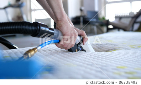Male Worker Cleaning a mattress With Vacuum Cleaner.Professionally extraction method. Upholstered furniture. Mattress chemical cleaning. 86238492