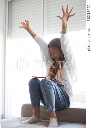 Overjoyed smiling teenage girl looking at phone screen, showing yes gesture close up, excited happy child celebrating success 86238662