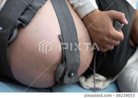 Close Up Pregnant Woman On Hospital Couch During Medical Control Cardiotocography. Visit Gynecologist Doctor At Clinic For Pregnancy Consultant. Examine Expectant Belly Baby Mother Healthcare Check Up 86239053