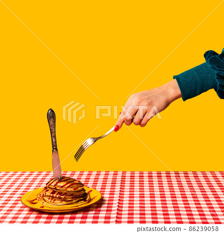 Food pop art photography. Female hand and sweet pancakes on plaid tablecloth isolated on bright yellow background. Vintage, retro style Food pop art photography. Female hand and sweet pancakes on plaid tablecloth isolated on bright yellow background. Vintage, retro style 86239058