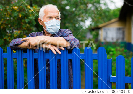 Old man in mask leaning on fence outdoors 86240968