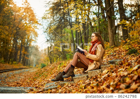 Young woman with book over autumn background Young woman with book over autumn background 86242798