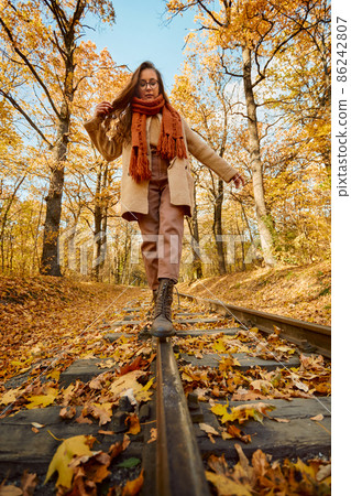 Woman balancing on railway over autumn background Woman balancing on railway over autumn background 86242807