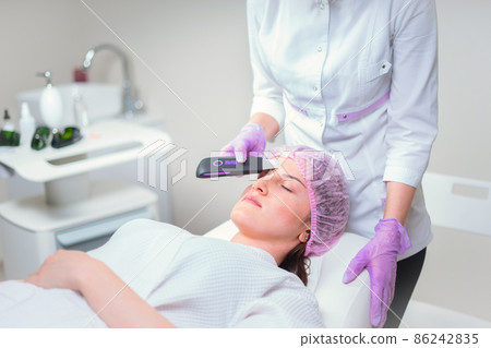 Hands of cosmetologist making ultrasound facial cleaning with special machine Hands of cosmetologist making ultrasound facial cleaning with special machine 86242835