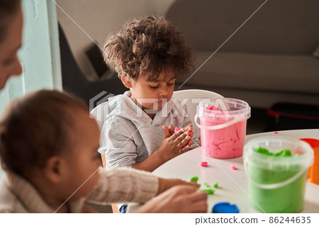 Concentrated brunette boy looking attentively and playing with purple sand on a white table 86244635