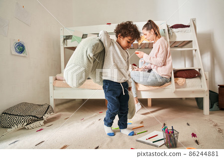 Child holding pillow and looking at the floor while playing at the room with his mother 86244881