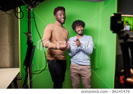 Two multiracial men sitting at the chair in front of the smartphone on the tripod 86245476