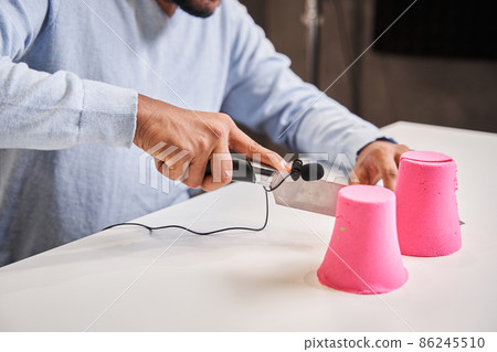 Pink molds from the kinetic sand standing at the table while male blogger chopping it Pink molds from the kinetic sand standing at the table while male blogger chopping it 86245510