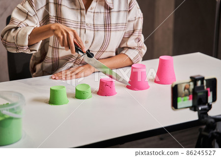 Multiracial woman holding knife and cutting kinetic sand while recording video 86245527
