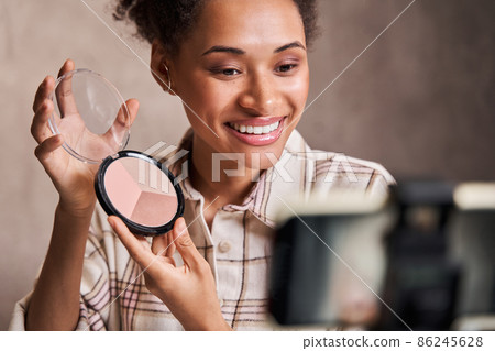 Multiracial woman showing blushes to the camera while recording make up tutorial 86245628