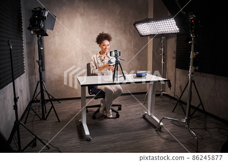 Multiracial female blogger holding some devices and sitting in front of the smartphone Multiracial female blogger holding some devices and sitting in front of the smartphone 86245877