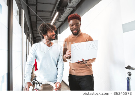 Multiracial stylish guy showing something at the screen of laptop to his male colleague Multiracial stylish guy showing something at the screen of laptop to his male colleague 86245878