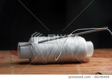 The thread is threaded through the eye of a sewing needle.Sewing and needlework classes.Workshop of hand craft and handmade.Workplace of the textile industry.The embroidery needle is stuck in a bobbin 86246409