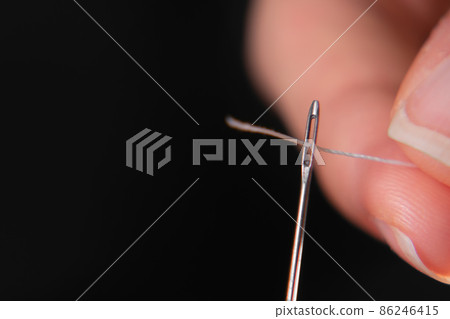 A hand threads a thread through the eye of a sewing needle. Sewing and needlework classes.Craft and handmade workshop.Workplace in the textile industry. Needle for embroidery by hand A hand threads a thread through the eye of a sewing needle. Sewing and needlework classes.Craft and handmade workshop.Workplace in the textile industry. Needle for embroidery by hand 86246415