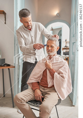 Satisfied grey haired male with towel at his shoulders smiling while looking at the mirror 86246537