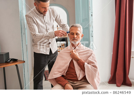 Concentrated adult man making haircut for his father at home with haircut machine 86246549