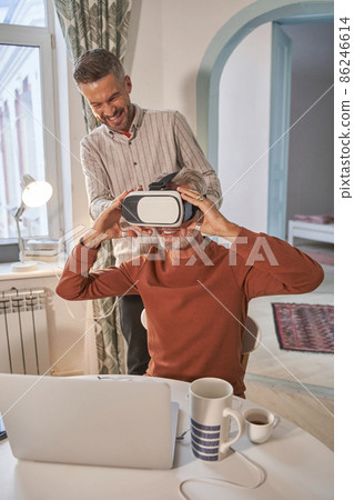 Handsome adult caucasian man adjusting his VR headset with toothy smile at his senior 86246614