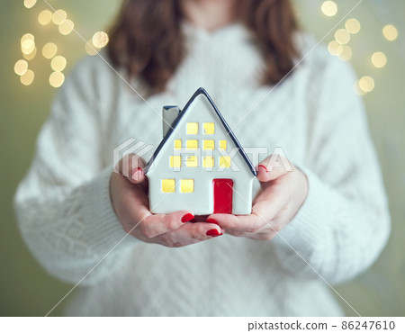 Woman holds in her hands ceramic house with light inside. The concept of holiday, christmas and coziness 86247610