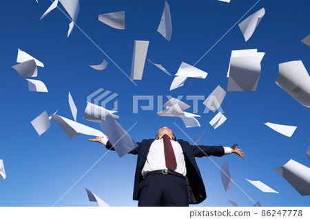 A man in a suit spreading his hands under the blue sky where documents dance 86247778