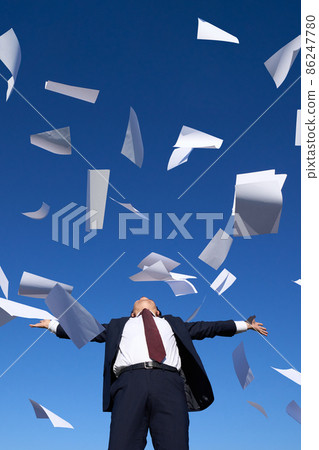 A man in a suit spreading his hands under the blue sky where documents dance A man in a suit spreading his hands under the blue sky where documents dance 86247780