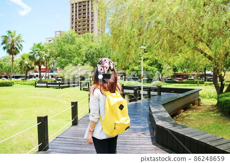 一個女性旅行者揹著鮮黃色的後背包站在公園橋上 一個女性旅行者揹著鮮黃色的後背包站在公園橋上 86248659