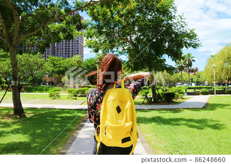 一個女性旅行者揹著鮮黃色的後背包站在公園 86248660