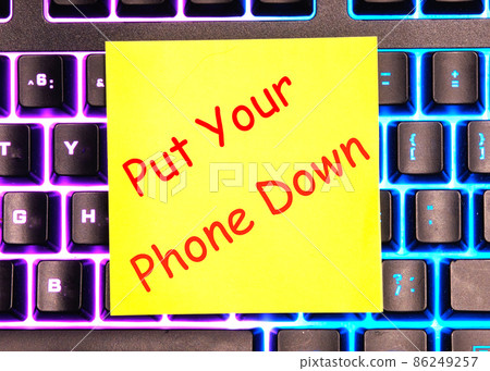 Put your phone down text written on a yellow sticker lies on a glowing keyboardbusiness 86249257