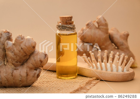 Glass bottle of essential ginger oil, ginger root on beige background. Healthy alternative living. Natural cosmetics ingredients for hair care. Wellness Eco comb Homemade hair mask treatment Glass bottle of essential ginger oil, ginger root on beige background. Healthy alternative living. Natural cosmetics ingredients for hair care. Wellness Eco comb Homemade hair mask treatment 86249288