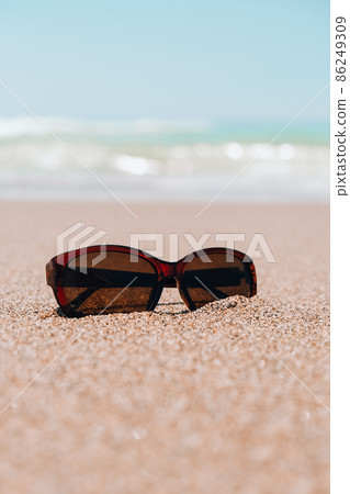 Sunglasses on the sand. Summer vacation concept. Protective sunglasses on sandy beach at tropical seaside on warm sunny day. Sunglasses on the sand. Summer vacation concept. Protective sunglasses on sandy beach at tropical seaside on warm sunny day. 86249309