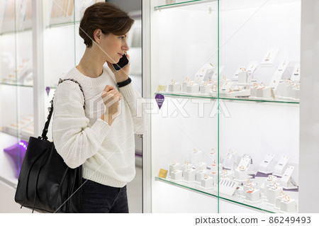 Young beautiful attractive brunette woman with a short haircut in a casual white sweater chooses Young beautiful attractive brunette woman with a short haircut in a casual white sweater chooses 86249493