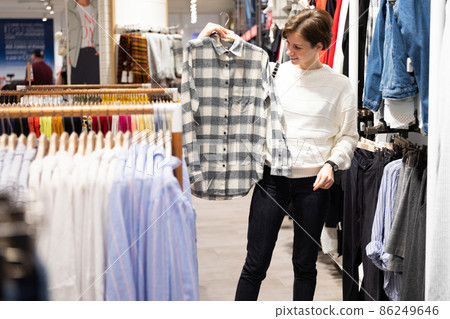 Photo of young attractive brunette woman with a short haircut in a white sweater chooses stylish and 86249646