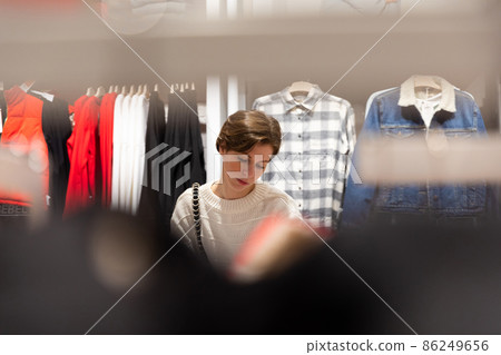 Young beautiful brunette woman with a short haircut in a white sweater chooses stylish clothes in a 86249656