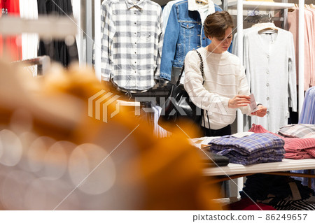 Young beautiful brunette woman with a short haircut in a white sweater chooses stylish clothes in a Young beautiful brunette woman with a short haircut in a white sweater chooses stylish clothes in a 86249657