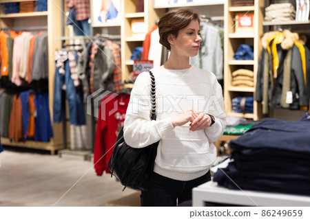 Young beautiful brunette woman with a short haircut in a white sweater chooses stylish clothes in a Young beautiful brunette woman with a short haircut in a white sweater chooses stylish clothes in a 86249659