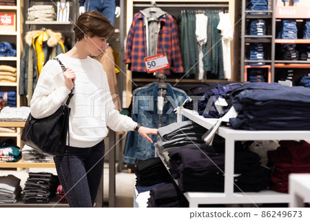 Young beautiful brunette woman with a short haircut in a white sweater chooses stylish clothes in a 86249673