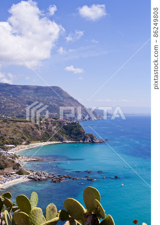 View of turquoise gulf bay, sandy beach, green mountains and plants, blue sky white clouds 86249808