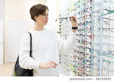 Photo of young thinking attractive brunette woman in a white sweater chooses glasses for vision on a Photo of young thinking attractive brunette woman in a white sweater chooses glasses for vision on a 86249885