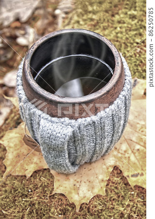Clay mug in woolen knitted cover. Steam from the mug Clay mug in woolen knitted cover. Steam from the mug 86250785