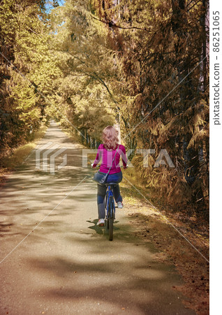 A girl on bicycle rides through in sunny autumn park. Rear view. A girl on bicycle rides through in sunny autumn park. Rear view. 86251065