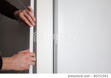 Mans hands installing protective decorative corner on the wall in apartment. Mans hands installing protective decorative corner on the wall in apartment. 86252041