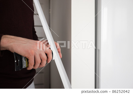 Mans hands glue decorative plastic corner on the wall in apartment. 86252042