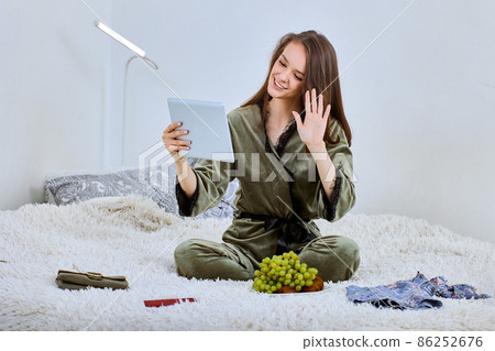 Web conference using tablet PC by happy woman who sits on bed indoors. 86252676