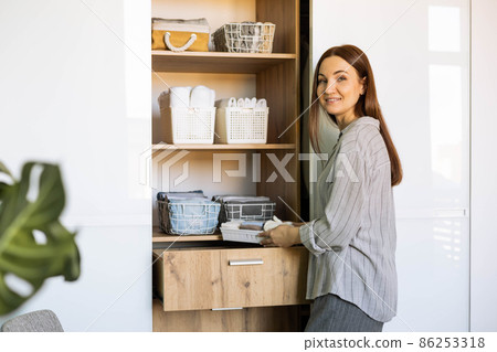 Smiling female putting clothes wardrobe comfortable vertical storage system Marie Kondo method Smiling female putting clothes wardrobe comfortable vertical storage system Marie Kondo method 86253318