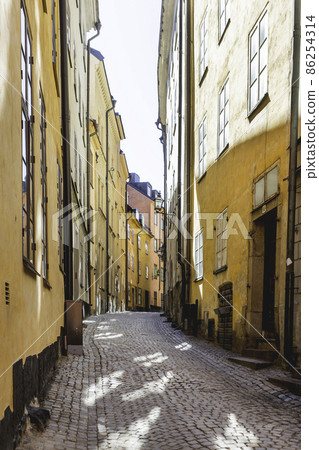 Bright sun reflections on narrow street in historic part of Stockholm. Old fashioned building in Gamla stan. Sweden. Bright sun reflections on narrow street in historic part of Stockholm. Old fashioned building in Gamla stan. Sweden. 86254314