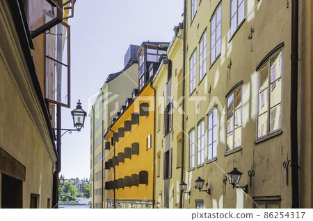 Bright sun reflections on narrow street in historical part of Stockholm. Old fashioned building in Gamla stan, old part of Stockholm, Sweden. Bright sun reflections on narrow street in historical part of Stockholm. Old fashioned building in Gamla stan, old part of Stockholm, Sweden. 86254317
