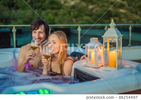 Portrait of young carefree happy smiling couple relaxing at hot tub during enjoying happy traveling moment vacation life against the background of green big mountains Portrait of young carefree happy smiling couple relaxing at hot tub during enjoying happy traveling moment vacation life against the background of green big mountains 86254497