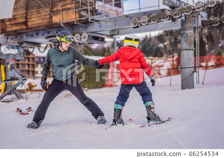 Boy learning to ski, training and listening to his ski instructor on the slope in winter Boy learning to ski, training and listening to his ski instructor on the slope in winter 86254534